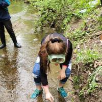Student stands in stream and grabs sample of water
